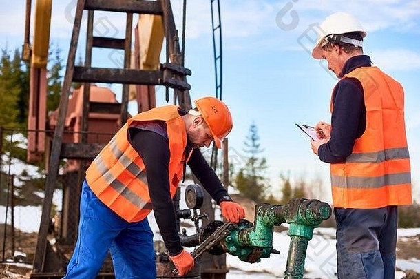 石油工人穿工作服橙色背心头盔工作石油场石油泵杰克痛苦的管使笔记概念石油行业协作