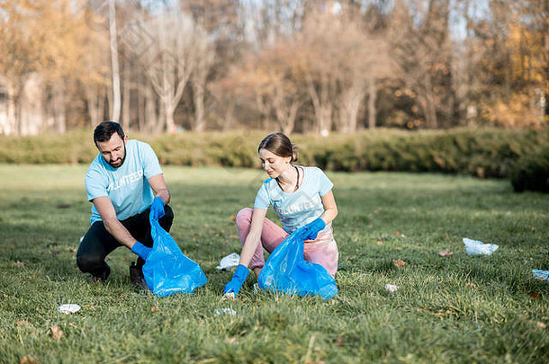 快乐男人。女人志愿者穿着蓝色的t恤清洁公共花园塑料垃圾袋