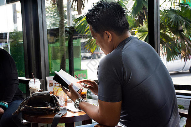 泰国男人。坐着放松阅读书会说话的喝冰咖啡咖啡馆商店11月Saraburi泰国