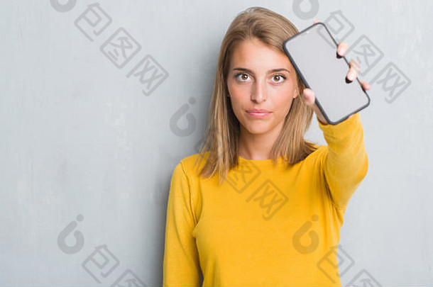 美丽的年轻的女人难看的东西灰色墙显示智能手机<strong>屏幕</strong>自信表达式聪明的脸思考