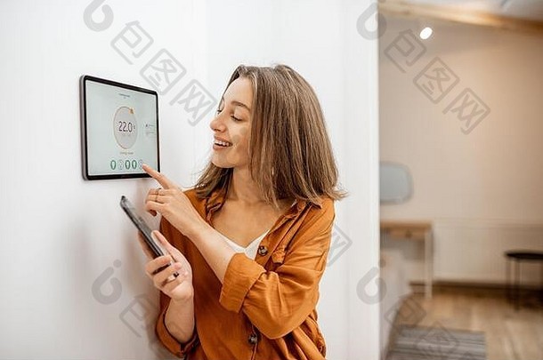 年轻的女人控制温度生活房间聪明的电话数字触摸屏幕面板概念加热控制聪明的首页