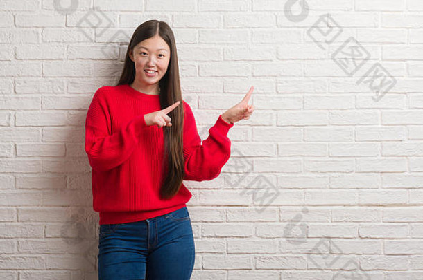 年轻的中国人女人砖墙微笑相机指出手手指一边