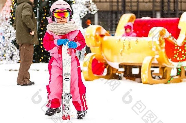 女孩穿护目镜头盔冬天假期在户外持有滑雪板相机微笑兴奋特写镜头模糊背景