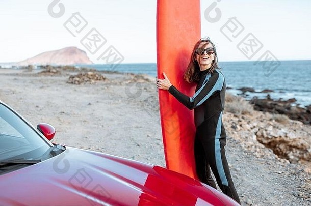 肖像年轻的女人冲浪者泳衣站冲浪板红色的车岩石海岸