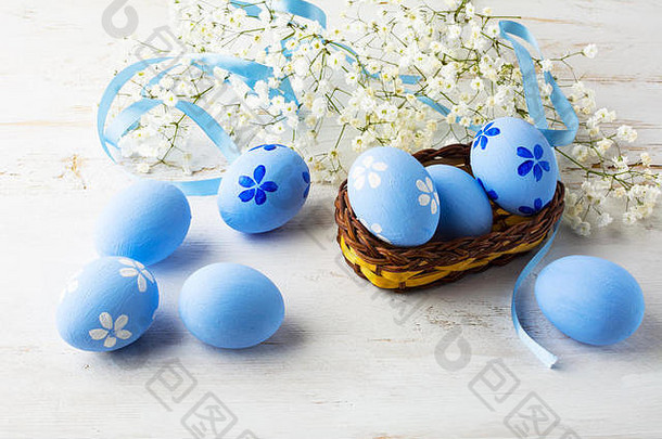蓝色的复活节鸡蛋小柳条篮子小白色婴儿的呼吸花白色木背景