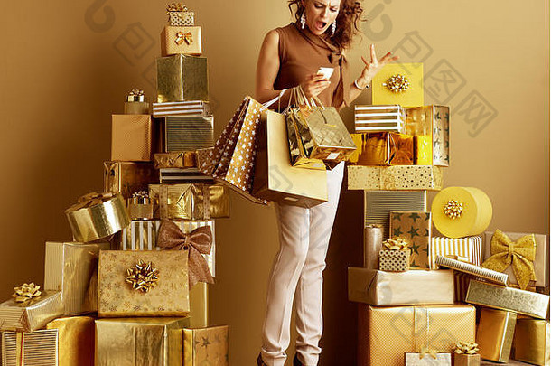 完整的长度肖像生气现代时尚迷黄金米色裤子棕色（的）上衣购物袋智能手机桩