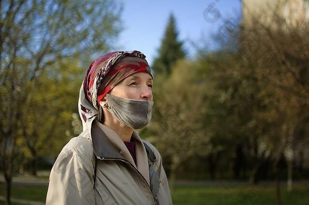 成熟的女人穿手工制作的纺织脸面具附件保护元素阳光明媚的春天一天公园冠状病毒