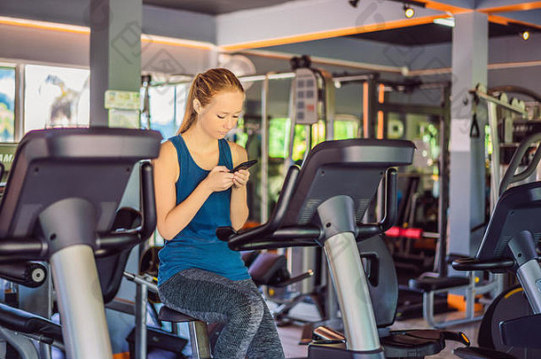 年轻的女人电话培训健身房女人坐着锻炼机持有移动电话