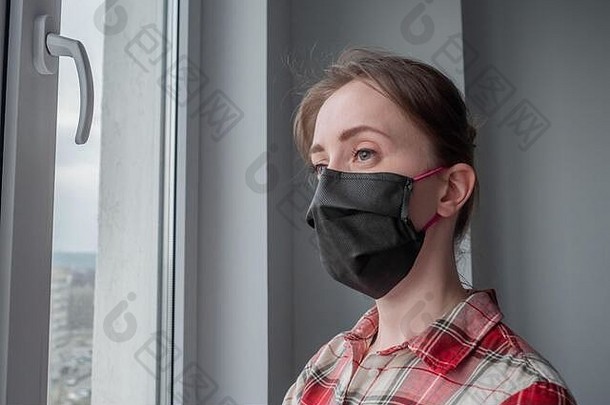 肖像沉思的女人穿黑色的医疗脸面具红色的格子衬衫窗口房间灰色墙首页隔离