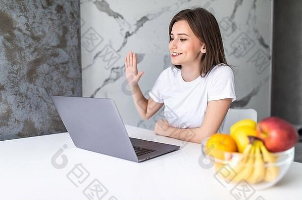 年轻的女人坐桌子上厨房视频调用现代电脑小工具女孩说话说话无线连接电脑咨询客户端