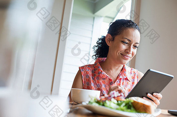 年轻的女人阅读屏幕数字平板电脑坐着表格咖啡三明治