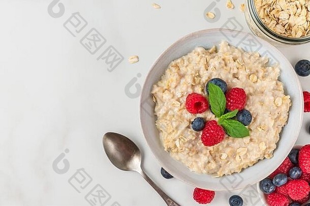 碗燕麦片粥新鲜的浆果薄荷服务勺子健康的饮食早餐白色表格前视图复制空间