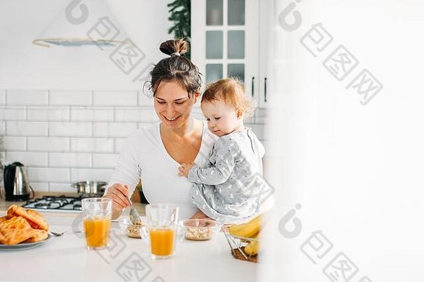 年轻的女人妈妈婴儿女孩手烹饪早餐明亮的厨房首页