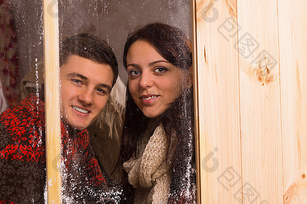 微笑年轻的夫妇站一边一边冷淡的窗口放冬天相机微笑