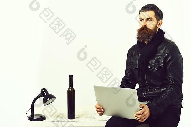 有胡子的男人。长胡子残酷的高加索人不剃须的赶时髦的人坐着表格灯瓶持有移动PC黑色的皮革夹克孤立的白色工作室背景复制空间