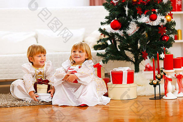 快乐双胞胎女孩坐着礼物盒子圣诞节树