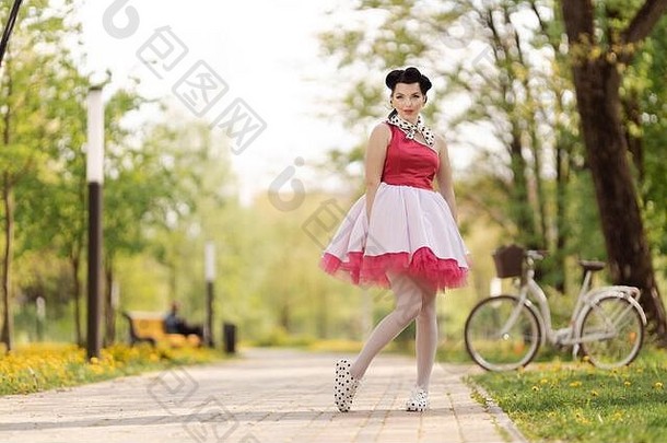 美丽的女孩粉红色的衣服发型风格舞蹈提出了公园阳光明媚的一天复古的风格照片