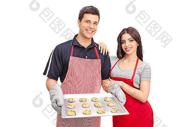 年轻的夫妇围裙持有锅巧克力芯片饼干相机孤立的白色背景