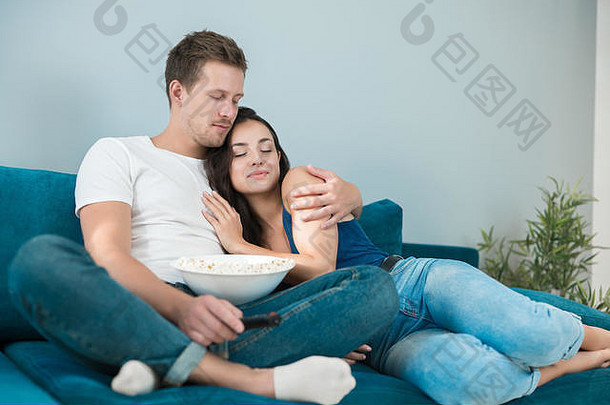 年轻的夫妇美丽的浅黑肤色的女人女人英俊的男人。看电影沙发生活房间吃流行玉米拥抱舒适的生活方式