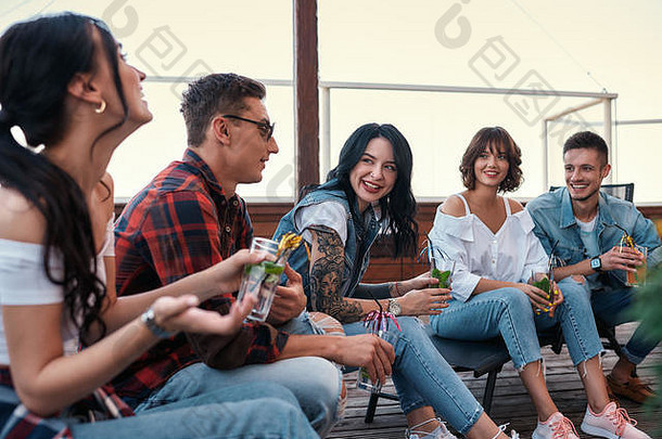 令人心寒的年轻的快乐的人聊天喝鸡尾酒坐着屋顶友谊概念