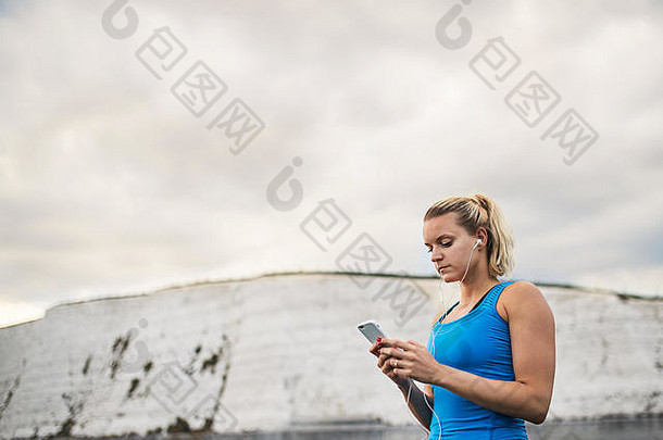 年轻的运动女人跑步者耳机智能手机站海滩