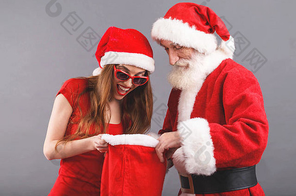圣诞老人老人白色胡子穿sungasses年轻的夫人老人穿圣诞老人他红色的衣服太阳镜站灰色的背景惊讶夫人圣诞老人搜索礼物圣诞老人老人袋一年圣诞节假期记忆礼物购物折扣商店雪少女圣诞老人老人化妆发型狂欢节