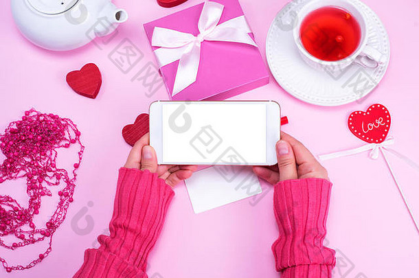女手持有智能手机空白色屏幕粉红色的表格背景杯茶盒子弓前视图м