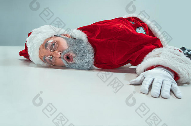 累了圣诞老人老人说谎地板上白色工作室背景男人。穿圣诞老人老人服装灰色的复制空间冬天销售