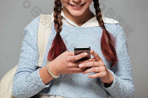 裁剪图像微笑女学生背包发短信移动电话站孤立的灰色的背景