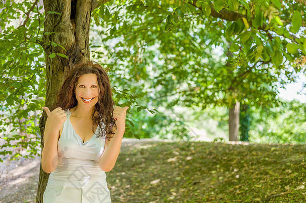 快乐的丰满的优雅的成熟的女人微笑相机显示拇指绿色花园背景复制空间