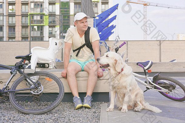 现代生活大城市运动年轻的男人。狗休息板凳上城市自行车骑