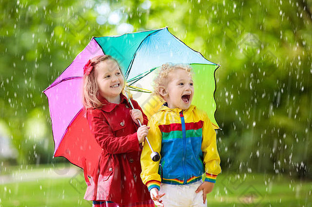 男孩女孩玩多雨的夏天公园孩子们色彩斑斓的彩虹伞防水夹克外套玩雨孩子们走