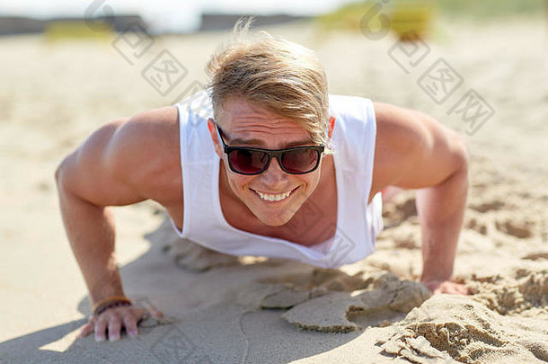 微笑年轻的男人。俯卧撑夏天海滩