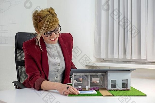 年轻的女架构师办公室坐着桌子上房子模型深思熟虑的设计师眼镜思考项目