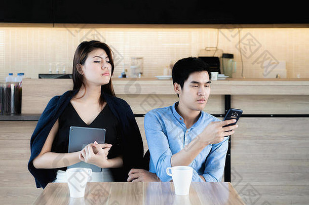 年轻的亚洲情人夫妇智能手机咖啡馆嫉妒女朋友窥视间谍男朋友的<strong>电话</strong>爱嫉妒概念
