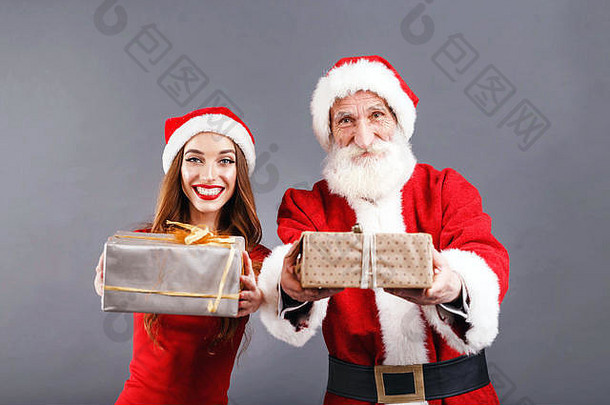 圣诞老人老人白色胡子穿sungasses年轻的夫人老人穿圣诞老人他红色的衣服太阳镜站灰色的背景持有礼物一年圣诞节假期记忆礼物购物折扣商店雪少女圣诞老人老人化妆发型狂欢节