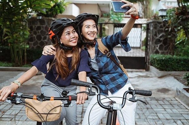 亚洲年轻的女人穿头盔袋相机手机使视频内容折叠自行车