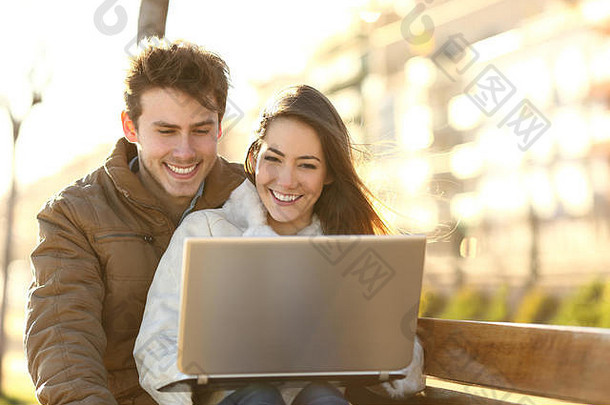 笑脸夫妇看媒体内容移动PC坐着板凳上公园
