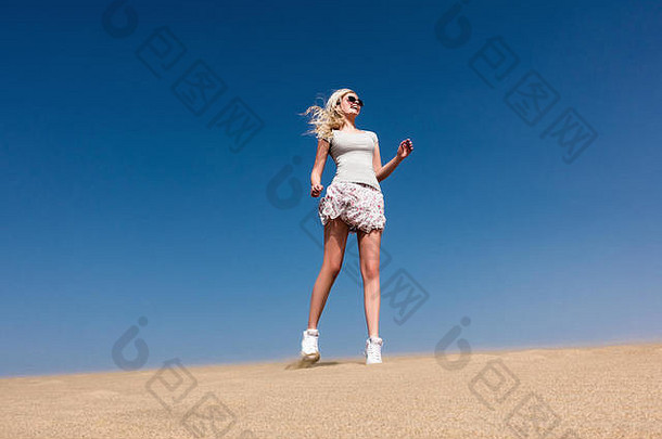 年轻的女孩穿裙子跳沙子沙漠