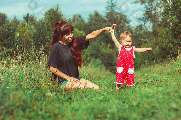 美丽的年轻的妈妈。女儿放松坐着草<strong>背景</strong>夏天草地绿色草树