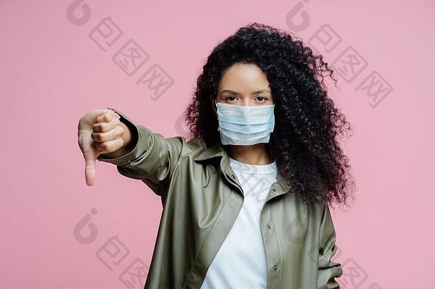 图像卷曲的头发的年轻的女人穿医疗面具拇指显示不喜欢手势避免了传播电晕病毒在乎
