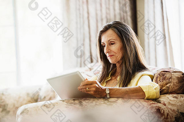 高级女人长棕色（的）头发坐着沙发数字平板电脑