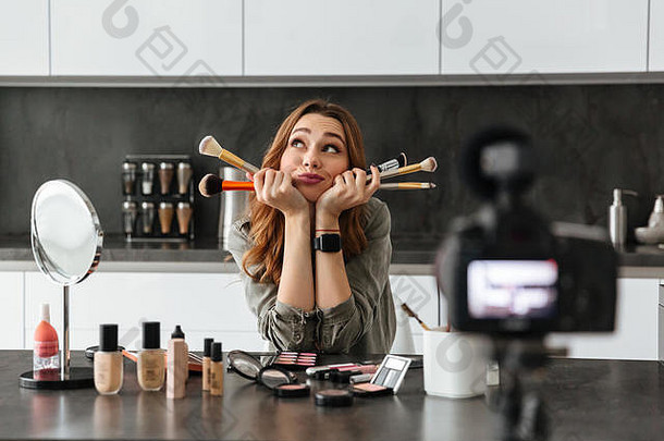 深思熟虑的年轻的女孩记录视频博客集化妆品产品坐着厨房表格首页应用化妆