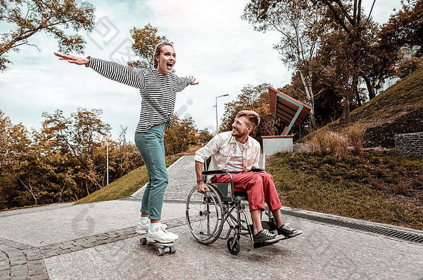 积极的男人。坐着轮椅女朋友骑滑板