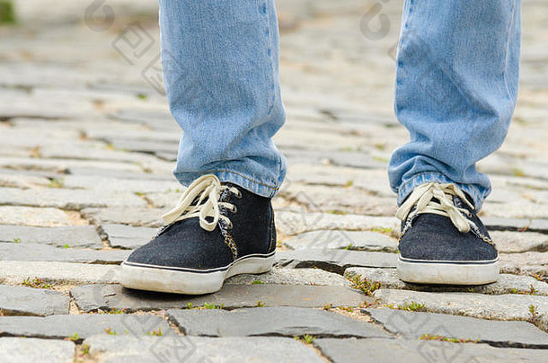 脚穿着蓝色的牛仔裤运动鞋男人。特写镜头石头人行道上