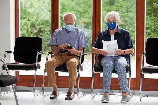高级夫妇坐着脸面具明亮的等待房间医院办公室男人。智能手机