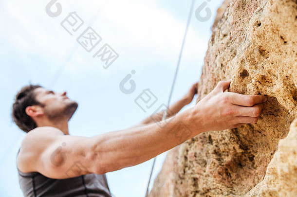 年轻的英俊的运动员攀爬岩石悬崖