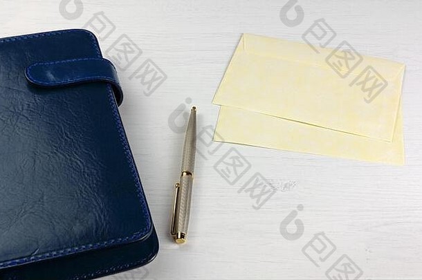 优雅的笔每天规划师蓝色的皮革封面黄色的信封白色木桌子上