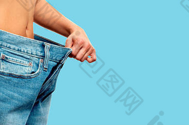 饮食概念重量损失女人超大的牛仔裤蓝色的背景