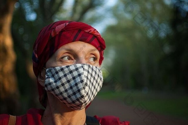 成熟的女人穿手工制作的纺织脸面具附件保护元素阳光明媚的春天一天公园冠状病毒